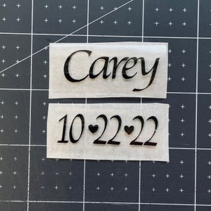 May include: Two pieces of white paper with black text. The top piece says "Carey" and the bottom piece says "10-22-22" with two small hearts between the numbers.