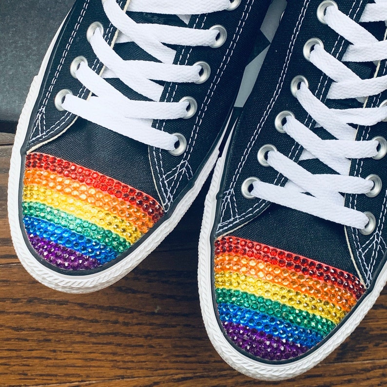 May include: A pair of black canvas sneakers with white laces and a rainbow-colored rhinestone design on the toe.