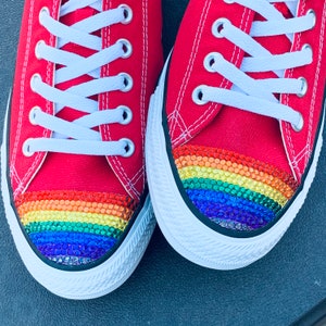 May include: A pair of red canvas sneakers with a rainbow-colored rhinestone trim on the toe.
