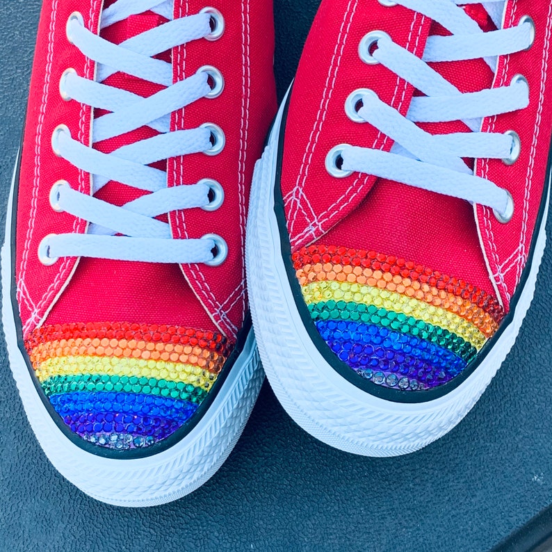 May include: A pair of red canvas sneakers with a rainbow-colored rhinestone trim on the toe.