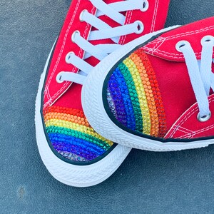 May include: A pair of red canvas sneakers with a rainbow-colored rhinestone design on the toe.