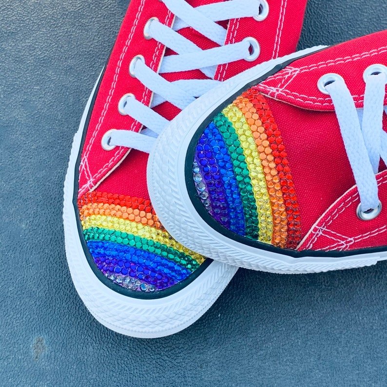 May include: A pair of red canvas sneakers with a rainbow-colored rhinestone design on the toe.
