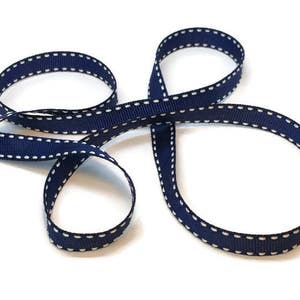 May include: Navy blue ribbon with white stitching. The ribbon is folded in a figure eight shape.