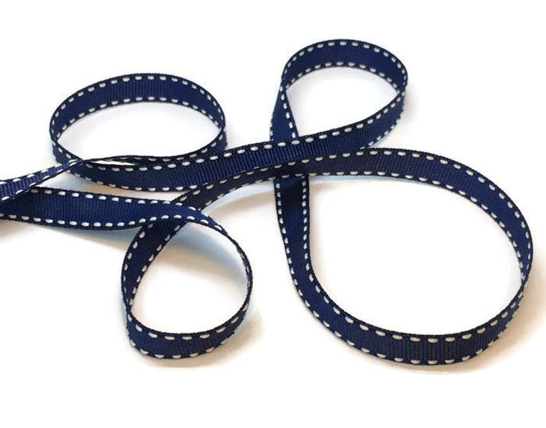 May include: Navy blue ribbon with white stitching. The ribbon is folded in a figure eight shape.