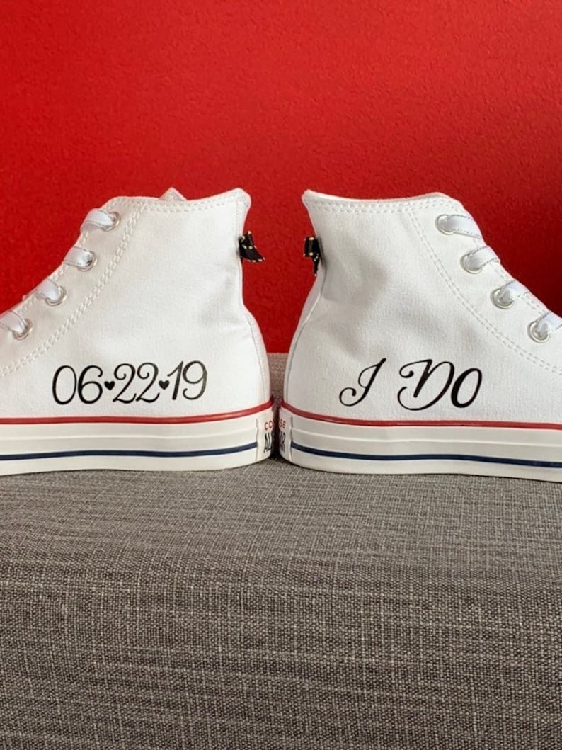Puede incluir: Un par de zapatillas blancas de ca&ntilde;a alta con cordones negros. Un zapato dice "06-22-19" con un s&iacute;mbolo de coraz&oacute;n y el otro zapato dice "S&iacute;, quiero".