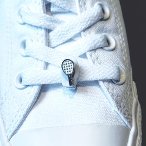 May include: White canvas trainers with white laces and a silver tennis racket shoe charm.