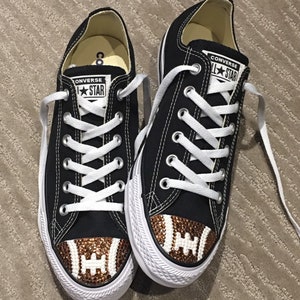 May include: A pair of black Converse All Star sneakers with brown and white rhinestones on the toe, forming the shape of a football.