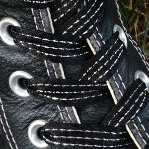 May include: Close-up of black leather shoe laces with silver glitter thread. The laces are threaded through silver eyelets.
