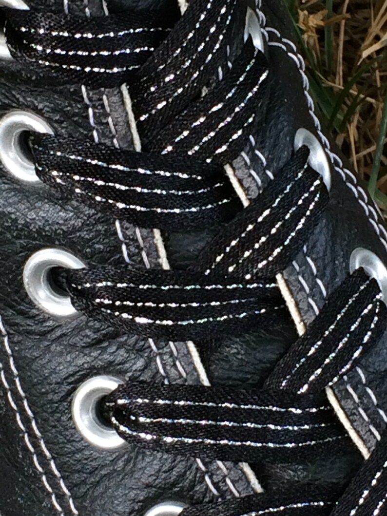 May include: Close-up of black leather shoe laces with silver glitter thread. The laces are threaded through silver eyelets.