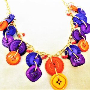 May include: A gold chain necklace with purple, orange, and yellow buttons. The buttons are various sizes and shapes.