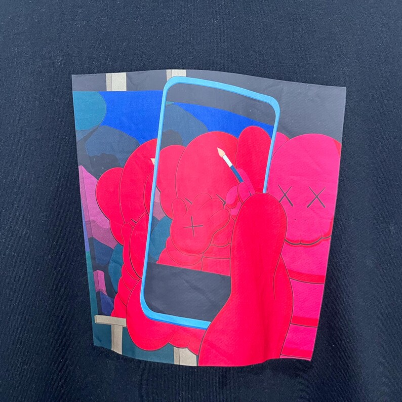 May include: A black sweatshirt featuring a graphic print of bright red cartoon figures with X-shaped eyes. A light blue rectangular frame resembling a smartphone screen overlays the figures, with one figure holding a small white paintbrush.