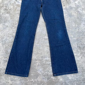 K&ouml;nnte beinhalten: Dunkelblaue Jeans aus Denim mit ausgestelltem Bein-Design. Die Jeans haben einen klassischen F&uuml;nf-Taschen-Stil und einen Knopf- und Rei&szlig;verschluss. Der Stoff scheint ein mittelschwerer Denim zu sein.