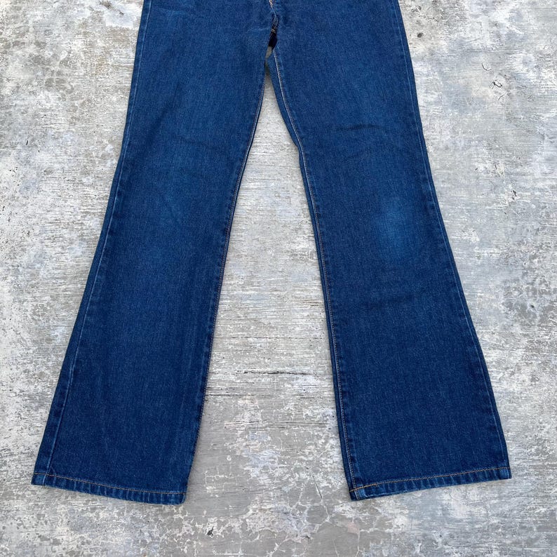 K&ouml;nnte beinhalten: Dunkelblaue Jeans aus Denim mit ausgestelltem Bein-Design. Die Jeans haben einen klassischen F&uuml;nf-Taschen-Stil und einen Knopf- und Rei&szlig;verschluss. Der Stoff scheint ein mittelschwerer Denim zu sein.