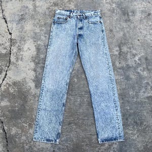 Może przedstawiać: Jasnoniebieskie dżinsy z efektem sprania kwasowego. Dżinsy mają zapięcie na guziki, pięć kieszeni i prostą nogawkę. Denim ma wyblakły, teksturowany wygląd.