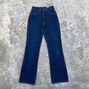 K&ouml;nnte beinhalten: Dunkelblaue Jeans mit hoher Taille und ausgestelltem Bein. Die Jeans haben ein klassisches F&uuml;nf-Taschen-Design und einen Knopf- und Rei&szlig;verschluss. Der Denim hat eine tiefe Indigo-Farbe, und die Jeans scheinen Vintage zu sein.