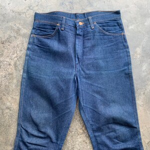 K&ouml;nnte beinhalten: Eine dunkelblaue Jeanshose. Die Jeans hat ein klassisches F&uuml;nf-Taschen-Design, einen Knopfverschluss und einen geraden Beinverlauf. Die N&auml;hte sind in einer kontrastierenden orange Farbe.