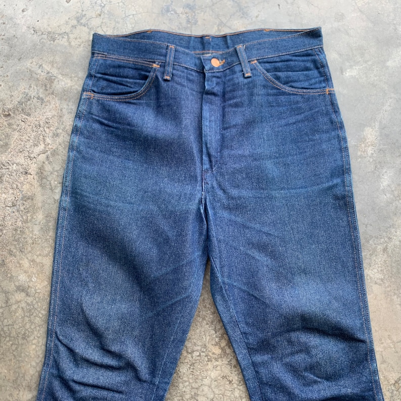 K&ouml;nnte beinhalten: Eine dunkelblaue Jeanshose. Die Jeans hat ein klassisches F&uuml;nf-Taschen-Design, einen Knopfverschluss und einen geraden Beinverlauf. Die N&auml;hte sind in einer kontrastierenden orange Farbe.
