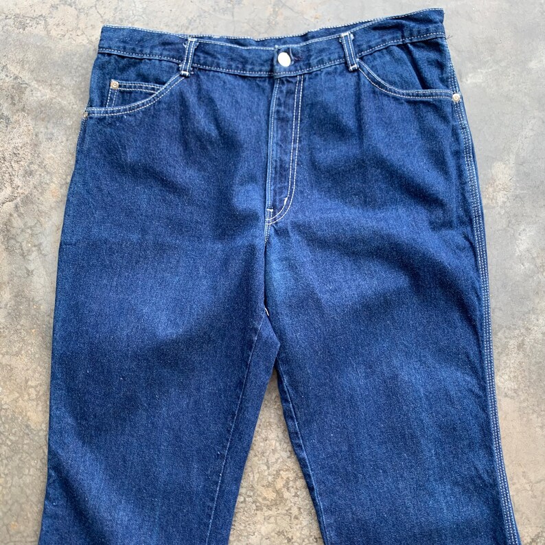 K&ouml;nnte beinhalten: Dunkelblaue Jeans aus Denim mit wei&szlig;en N&auml;hten. Die Jeans haben einen Knopfverschluss, Vordertaschen und Ges&auml;&szlig;taschen. Ein klassischer Stil, geeignet f&uuml;r den Alltag.