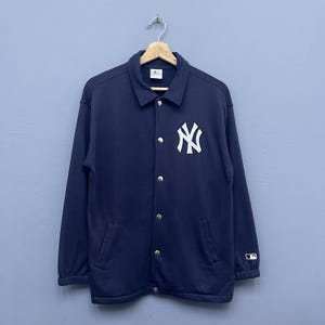 Può includere: Giacca blu navy con bottoni con il logo dei New York Yankees in bianco sul petto a sinistra. La giacca ha un collo, maniche lunghe e due tasche anteriori. Un piccolo logo MLB è sulla manica destra.