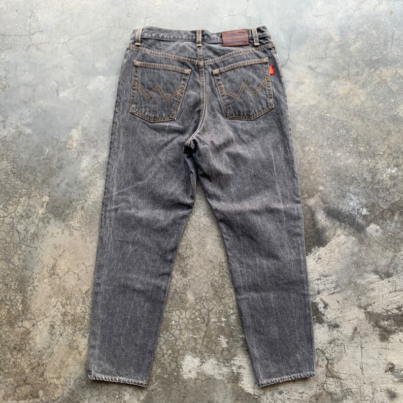 May include: A pair of faded black denim jeans. The jeans have a classic five-pocket design with a straight leg cut. The back pockets feature a distinctive stitched design. A small red tag is visible on the back pocket.