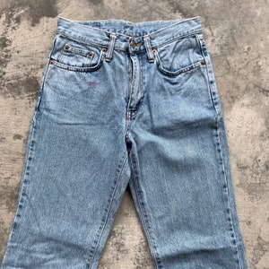K&ouml;nnte beinhalten: Hellblaue Jeans mit klassischem F&uuml;nf-Taschen-Design. Die Jeans haben einen Knopf- und Rei&szlig;verschluss, kupferfarbene Nieten und einen kleinen roten Fleck in der N&auml;he der Vordertasche. Vintage-Stil.