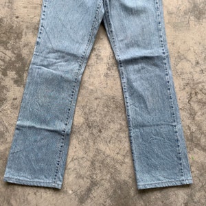 K&ouml;nnte beinhalten: Hellblaue Jeans mit klassischem geradem Bein. Die Jeans bestehen aus strapazierf&auml;higem Denim-Material und verf&uuml;gen &uuml;ber ein traditionelles F&uuml;nf-Taschen-Design. Die Jeans liegen flach auf einer grauen Oberfl&auml;che.