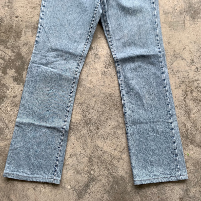 K&ouml;nnte beinhalten: Hellblaue Jeans mit klassischem geradem Bein. Die Jeans bestehen aus strapazierf&auml;higem Denim-Material und verf&uuml;gen &uuml;ber ein traditionelles F&uuml;nf-Taschen-Design. Die Jeans liegen flach auf einer grauen Oberfl&auml;che.