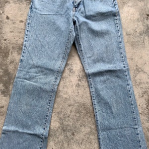 K&ouml;nnte beinhalten: Hellblaue Jeans mit klassischem F&uuml;nf-Taschen-Design. Die Jeans haben eine gerade Beinpassform und bestehen aus strapazierf&auml;higem Denim-Stoff. Die Jeans liegen flach auf einer Betonoberfl&auml;che.