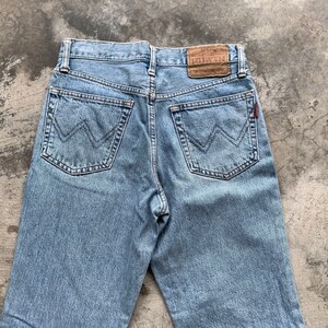 K&ouml;nnte beinhalten: Hellblaue Jeans mit dem Markennamen "EDWIN" auf einem braunen Lederpatch. Die Jeans hat zwei Ges&auml;&szlig;taschen mit einem markanten "W"-Nahtdesign. Ein kleines rotes Etikett ist auf der rechten Ges&auml;&szlig;tasche sichtbar.