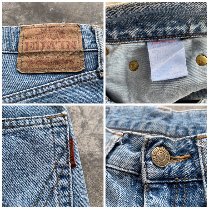 K&ouml;nnte beinhalten: Nahaufnahmen von hellblauen Jeans. Details sind ein Lederpatch mit "EDWIN"-Branding, Metallnieten, ein rotes Etikett auf der Ges&auml;&szlig;tasche und ein Knopfverschluss. Die Jeans weisen Gebrauchsspuren auf.