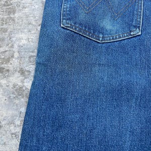 May include: Close-up of a section of blue denim jeans. The image shows the texture of the fabric and a back pocket with a decorative stitch design. The jeans are a medium wash.
