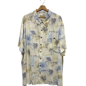 May include: A short-sleeved button-down shirt with a tropical print featuring palm trees and fish in shades of blue, green, and beige. The shirt is hanging on a wooden hanger against a white background.