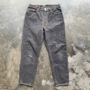 May include: A pair of faded black denim jeans. The jeans have a classic five-pocket design, a button and zipper closure, and a straight leg cut. The denim has a worn, textured appearance.