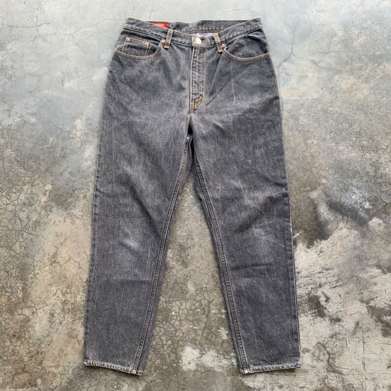May include: A pair of faded black denim jeans. The jeans have a classic five-pocket design, a button and zipper closure, and a straight leg cut. The denim has a worn, textured appearance.