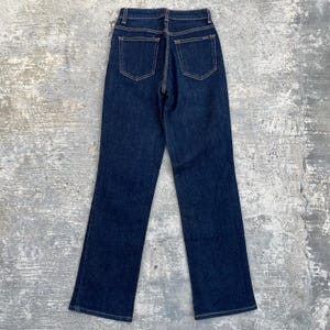 May include: Dark wash denim jeans with a classic five-pocket design. The jeans feature a high waist and a straight leg cut. The back view shows the pockets and the stitching details. The jeans are made of a sturdy denim material.