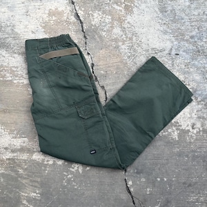 May include: Green cargo pants with multiple pockets and a belt loop. The pants are made of a durable fabric and have a relaxed fit. The pants are laid out on a concrete surface.