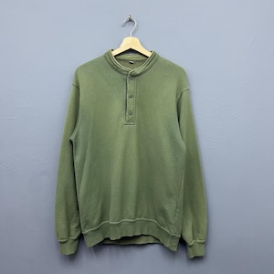 May include: Olive green long-sleeve sweatshirt with a button-up collar. The sweatshirt has a ribbed hem and cuffs. The garment is hanging on a wooden hanger against a gray background.