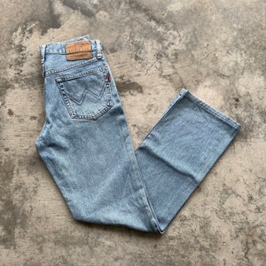 K&ouml;nnte beinhalten: Hellblaue Jeans mit klassischem F&uuml;nf-Taschen-Design. Die Jeans haben einen geraden Bein-Schnitt und einen braunen Lederaufn&auml;her am hinteren Bund. Die Ges&auml;&szlig;tasche hat ein markantes Nahtdesign. Die Jeans sind auf einer grauen Oberfl&auml;che gefaltet.