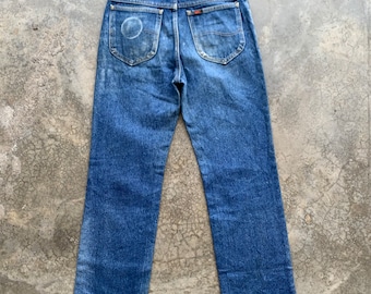 May include: Vintage blue denim jeans with the Lee brand label on the back waistband. The jeans have a classic five-pocket design and a straight leg cut. The back pockets show wear and a faded circular mark.