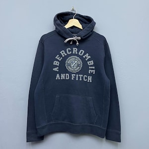 May include: Navy blue hooded sweatshirt with the text "Abercrombie & Fitch" in a circular design on the front. The sweatshirt has a kangaroo pocket and a drawstring hood. The logo is in a distressed, vintage style.