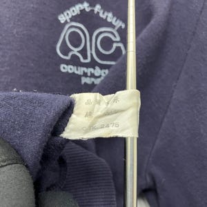 May include: Close-up of a navy blue garment with white text and logo. The text reads "sport futur" above a stylized "AC" logo and "courr&egrave;ges paris" below. A white tag displays Japanese characters and "TK 2475".