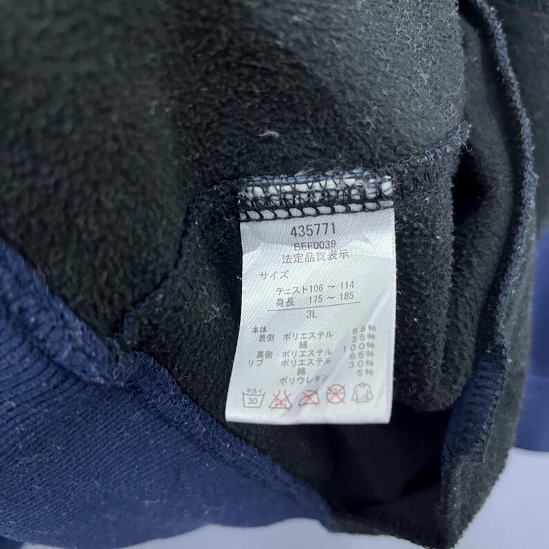Puede incluir: Primer plano de una prenda negra y azul marino con una etiqueta. La etiqueta muestra el n&uacute;mero 435771, la talla 3L y texto japon&eacute;s con medidas de pecho y altura. La tela es de poli&eacute;ster y poliuretano.