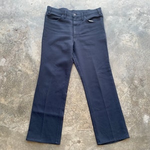 Peut inclure: Pantalon bleu marine foncé avec une coupe droite classique. Le pantalon est doté d'une fermeture boutonnée et zippée, ainsi que de poches avant et arrière. Le tissu semble être un matériau durable de poids moyen, adapté au quotidien.