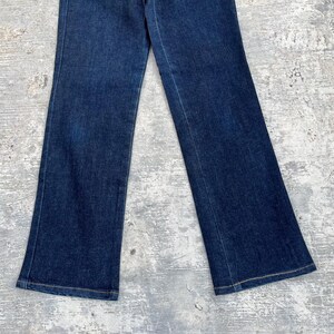 May include: Dark wash denim jeans with a slight flare at the hem. The jeans have a classic five-pocket design and a button and zipper closure. The fabric appears to be a medium-weight denim.