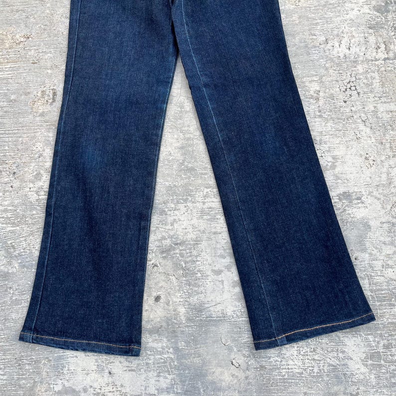May include: Dark wash denim jeans with a slight flare at the hem. The jeans have a classic five-pocket design and a button and zipper closure. The fabric appears to be a medium-weight denim.