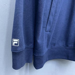 Puede incluir: Sudadera con capucha azul marino con un logotipo blanco y azul marino en la manga izquierda. La sudadera tiene una capucha con cord&oacute;n y un bolsillo de canguro. La tela parece ser un material suave y de peso medio.