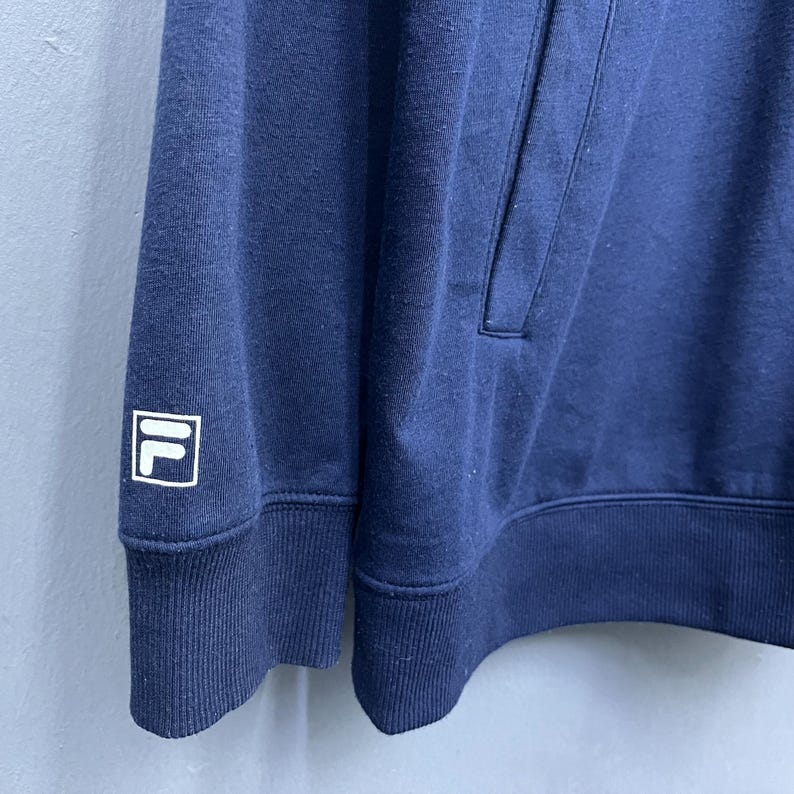 Puede incluir: Sudadera con capucha azul marino con un logotipo blanco y azul marino en la manga izquierda. La sudadera tiene una capucha con cord&oacute;n y un bolsillo de canguro. La tela parece ser un material suave y de peso medio.