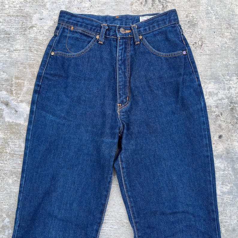 K&ouml;nnte beinhalten: Dunkelblaue Jeans aus Denim mit hohem Bund und klassischem F&uuml;nf-Taschen-Design. Die Jeans haben einen Knopf- und Rei&szlig;verschluss sowie kupferfarbene Nieten und N&auml;hte. Der Denim hat ein leicht verwaschenes Aussehen.