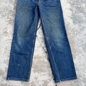 Pode incluir: Cal&ccedil;as de ganga azuis com um corte reto cl&aacute;ssico. As cal&ccedil;as de ganga mostram sinais de desgaste, com &aacute;reas desbotadas e desgaste subtil. A cor geral &eacute; azul m&eacute;dio, com um design tradicional de cinco bolsos e um fecho de bot&atilde;o e fecho de correr.