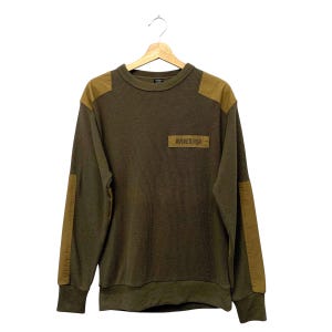 May include: An olive green long-sleeve crewneck sweater with a waffle-knit texture. It features tan fabric panels on the shoulders and along the outer sleeves. A rectangular patch on the left chest displays the text AVIREX USA in dark lettering.